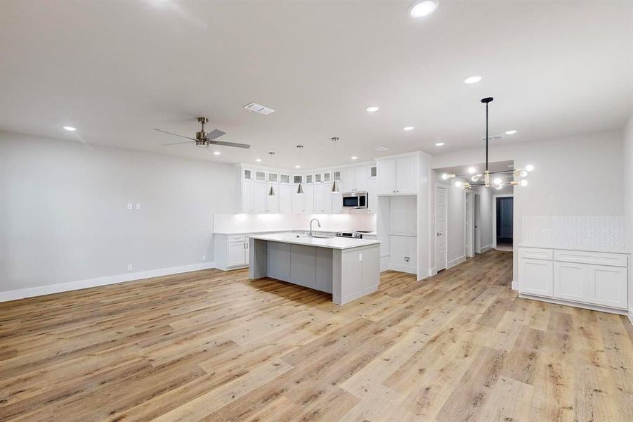 Kitchen featuring pendant lighting, white cabinets, ceiling fan, light wood-type flooring, and an island with sink