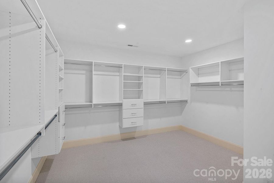 A spacious walk-in closet featuring custom solid shelving—NO WIRE SHELVING—designed for both beauty and organization.