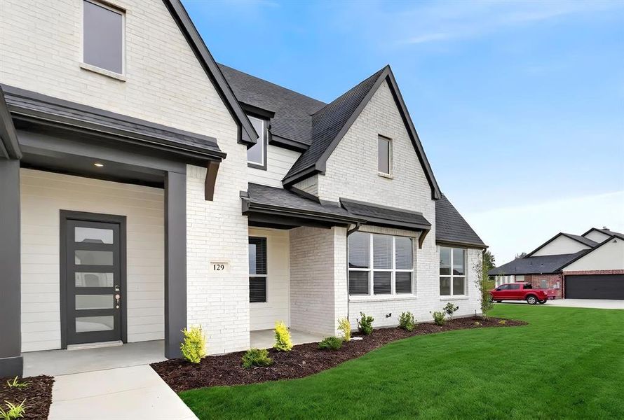 Contemporary exterior featuring white brick and siding, a dark gray entry door with multiple glass panes, black-trimmed windows, a dark shingle roof, and a meticulously manicured lawn Contemporary exterior featuring white brick and siding, a dark gray entry door with multiple glass panes, black-trimmed windows, a dark shingle roof, and a meticulously manicured lawn