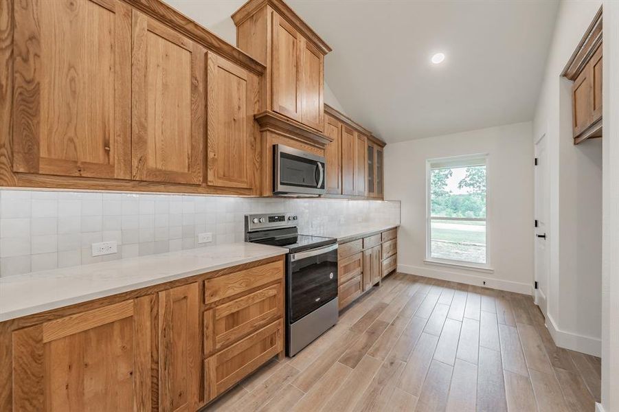 Kitchen with stainless steel appliances, baseboards, backsplash, light wood-type flooring, and vaulted ceiling