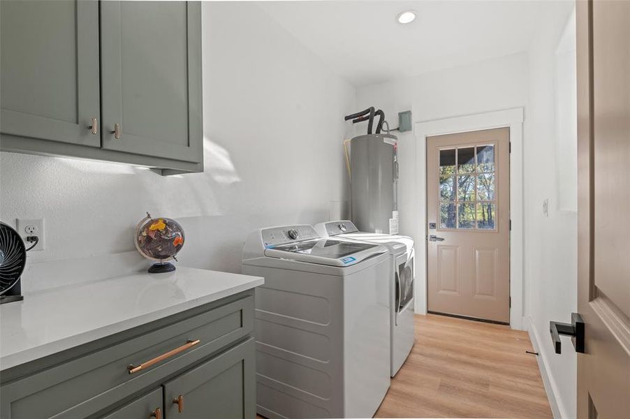 Laundry area featuring cabinets, electric water heater, light hardwood / wood-style floors, and washer and dryer