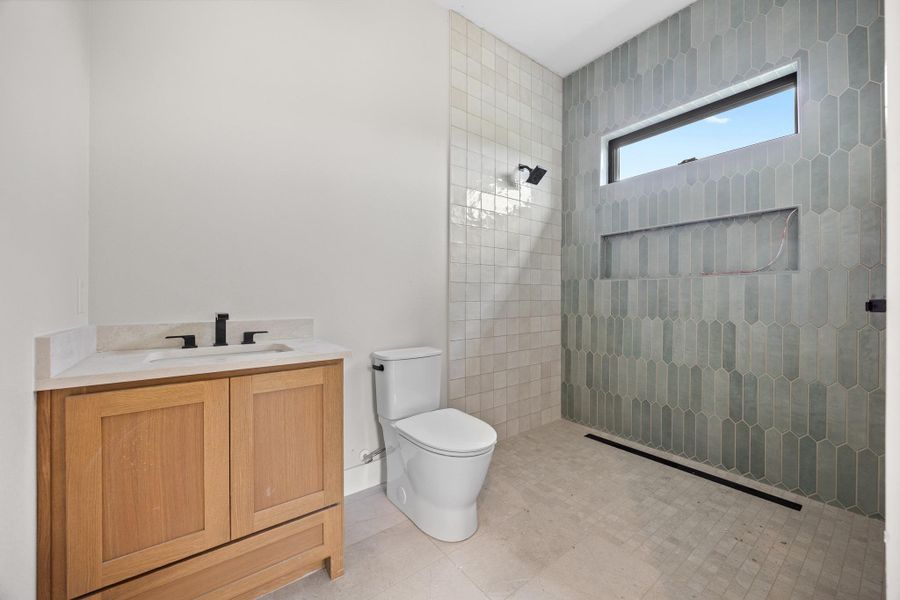 Modern bathroom featuring a wood-finish vanity with a light-colored countertop, matte black fixtures, a contemporary toilet, a shower with floor-to-ceiling tile, and a rectangular window