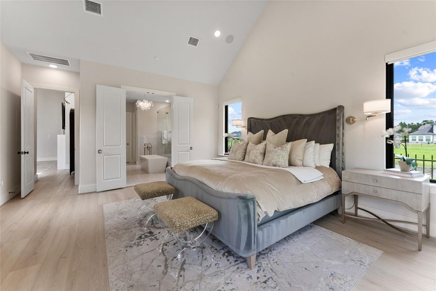 The primary bedroom is positioned for separation and calm, with large windows and a soft neutral palette. The scale of the room allows for both rest and a relaxed sitting area.
