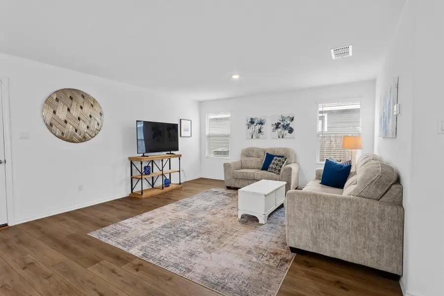 Open-concept living area featuring wood-finish flooring, white walls, recessed lighting, and multiple windows with blinds