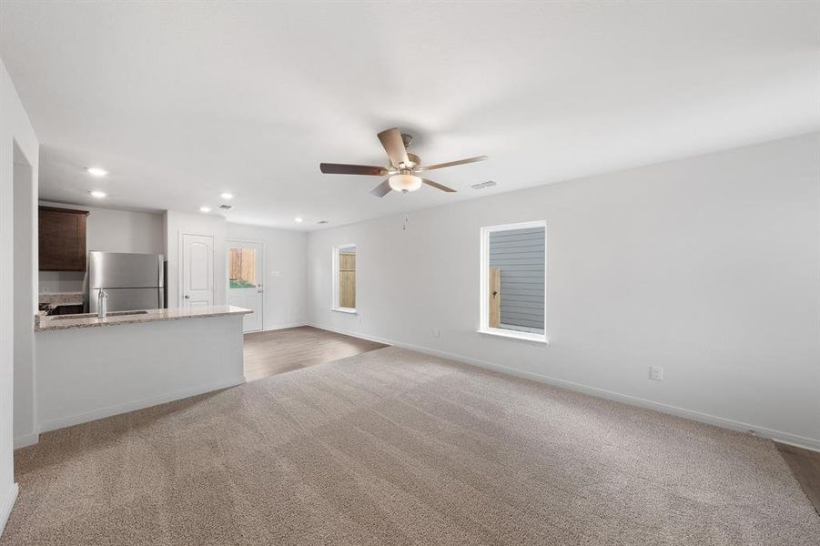 Unfurnished living room featuring sink, light carpet, and ceiling fan