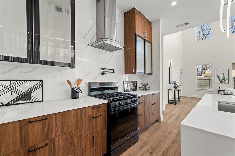Kitchen featuring wood finish cabinetry, range with gas cooktop, range hood, light stone counters, and backsplash