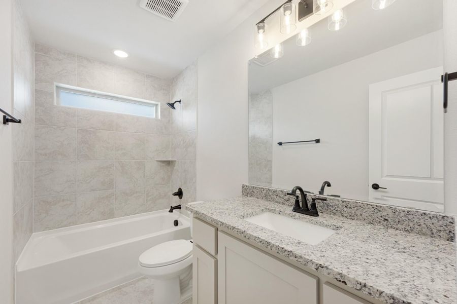 Bathroom with granite vanity, tub-shower combo with tile surround, and black fixtures