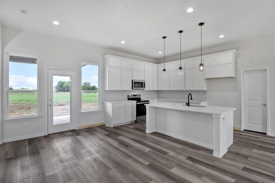 Kitchen with white cabinets, backsplash, a kitchen island with sink, wood-type flooring, and appliances with stainless steel finishes