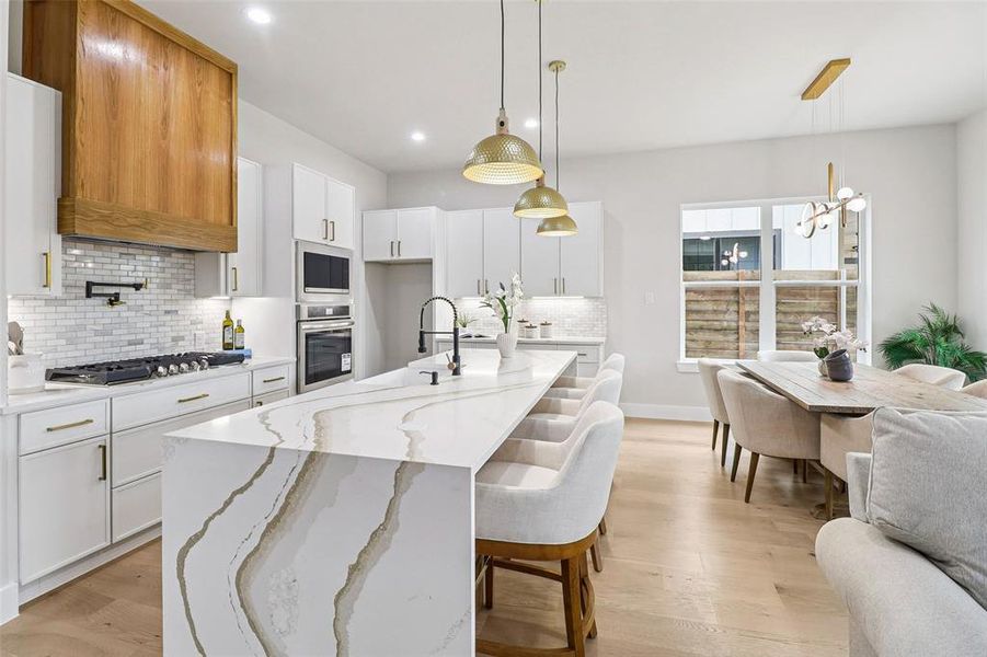 Kitchen with light stone countertops, open floor plan, light wood-type flooring, white cabinets, and a center island with sink