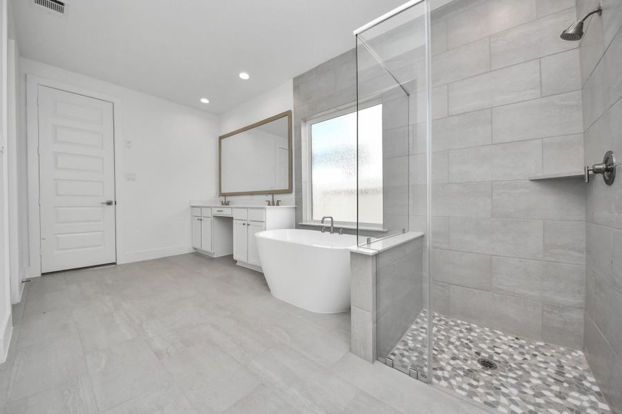 Escape to a spa-like oasis in this primary bathroom. Enjoy a walk-in shower with tile surround, a separate garden tub with custom detailing, and an elegant vanity featuring light countertops, modern hardware, and beautiful recessed lights. Experience luxury and relaxation in every detail.