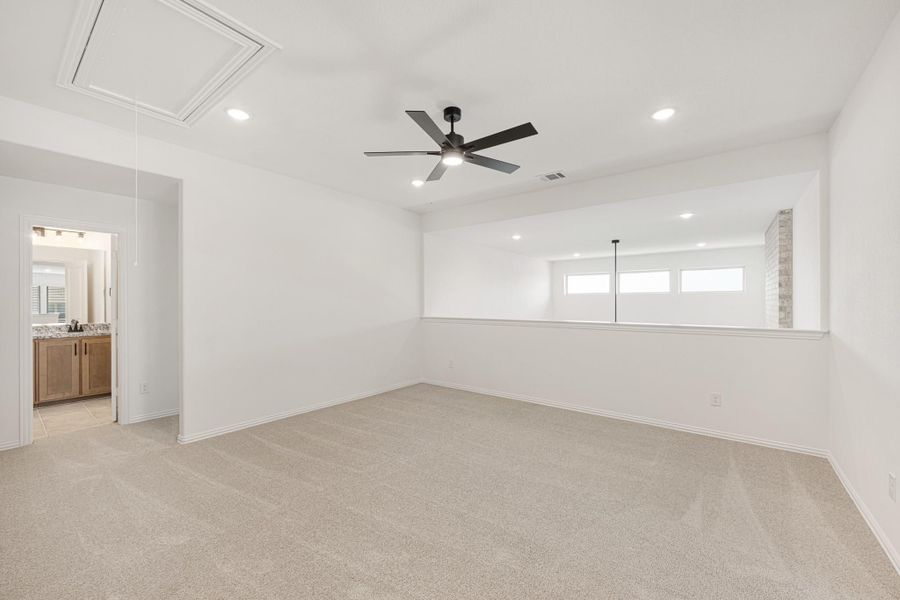 Spacious bedroom with beige carpet, ceiling fan, recessed lighting, and ensuite bathroom doorway visible. Spacious bedroom with beige carpet, ceiling fan, recessed lighting, and ensuite bathroom doorway visible.