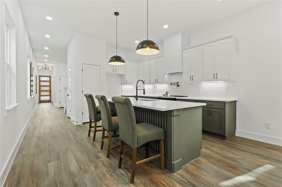 Two tone kitchen featuring dual tone cabinets, a kitchen bar, a center island with sink, decorative light fixtures, and dark wood-style floors