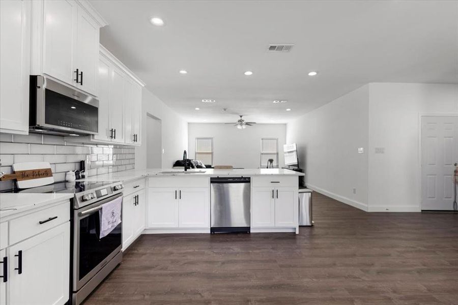 Kitchen featuring stainless steel appliances, white cabinetry, dark wood-style flooring, recessed lighting, and decorative backsplash Kitchen featuring stainless steel appliances, white cabinetry, dark wood-style flooring, recessed lighting, and decorative backsplash