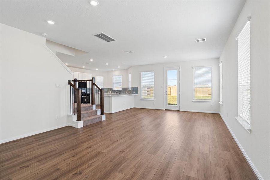 Another view of the open floor plan showcasing the gorgeous vinyl plank flooring, dining room, kitchen, and staircase leading to the second floor.