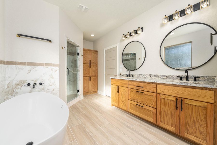 Bathroom featuring a freestanding bath, double vanity, a marble finish shower, wood tiled floors, and tile walls Bathroom featuring a freestanding bath, double vanity, a marble finish shower, wood tiled floors, and tile walls