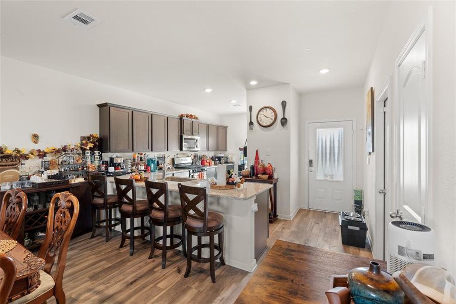 Kitchen featuring a peninsula, light wood finished floors, a kitchen breakfast bar, light stone countertops, and dark brown cabinets