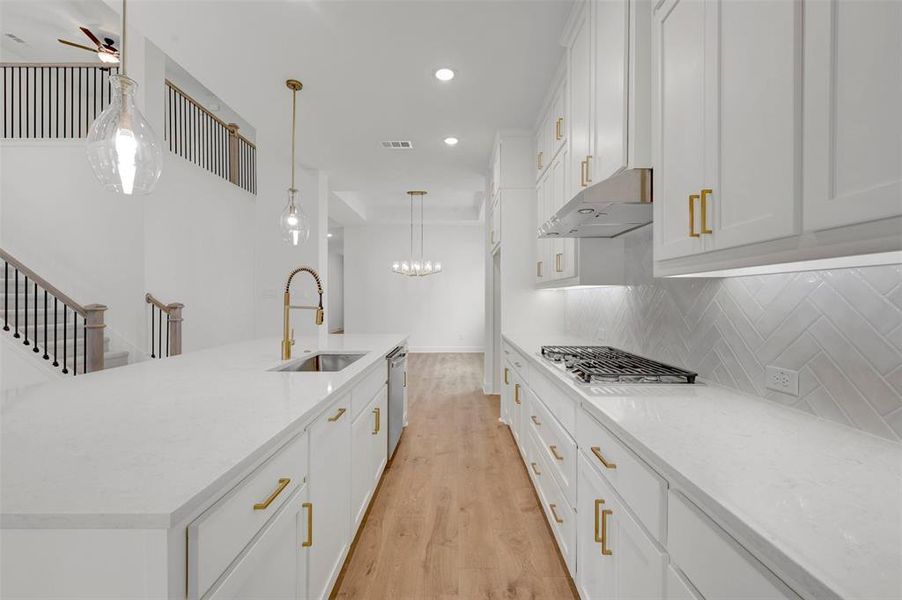The gourmet kitchen features white cabinetry with gold hardware, white countertops, and a gas cooktop