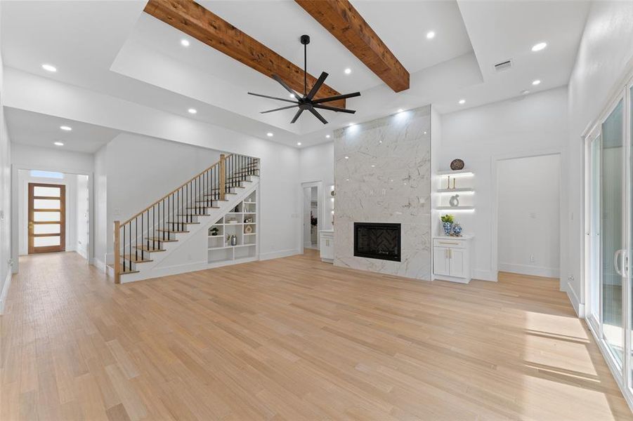Unfurnished living room with beam ceiling, light wood-type flooring, stairs, a ceiling fan, and a high end fireplace