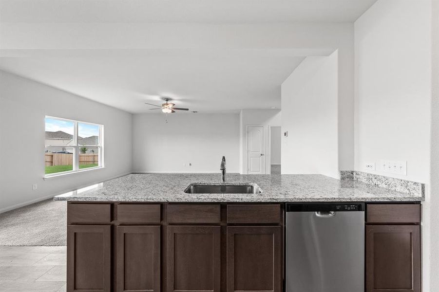 Kitchen featuring dishwasher, sink, ceiling fan, light stone countertops, and dark brown cabinets