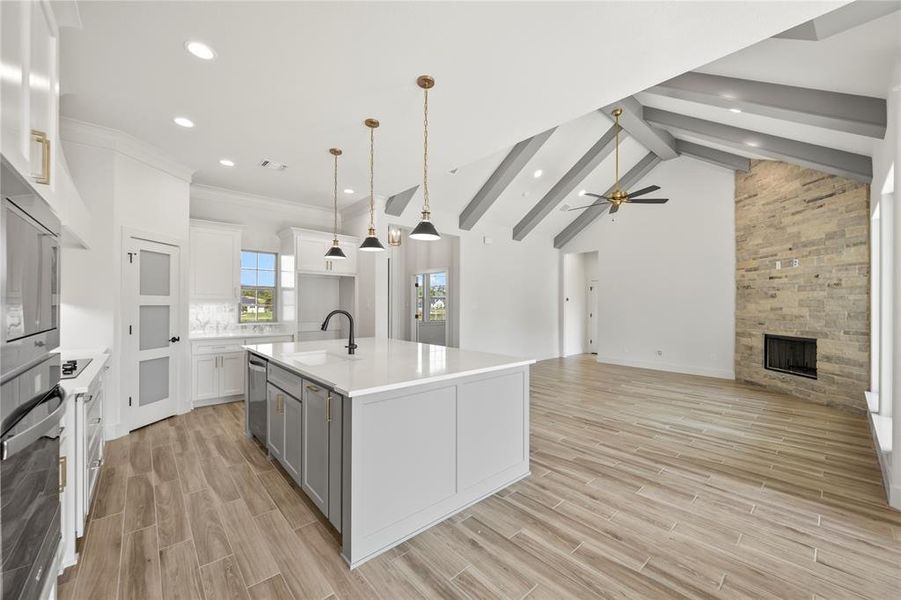 Kitchen featuring pendant lighting, an island with sink, a fireplace, wood tiled floors, and appliances with stainless steel finishes