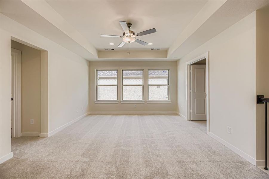 Empty room with light carpet, a tray ceiling, and ceiling fan Empty room with light carpet, a tray ceiling, and ceiling fan