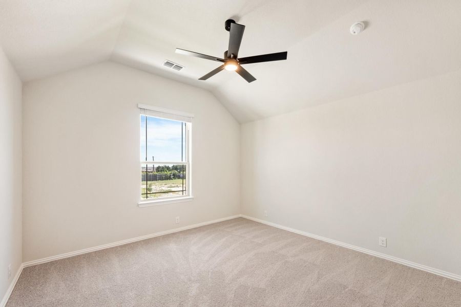 Empty bedroom with vaulted ceiling, black ceiling fan, carpet flooring, and a single window with backyard view Empty bedroom with vaulted ceiling, black ceiling fan, carpet flooring, and a single window with backyard view