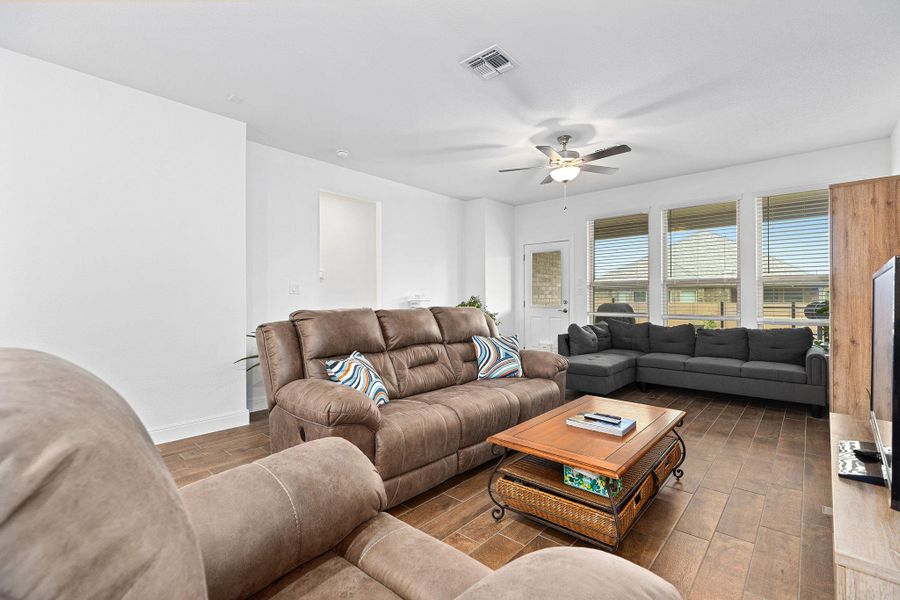 Well-lit living area featuring rich wood-look flooring and a functional ceiling fan.