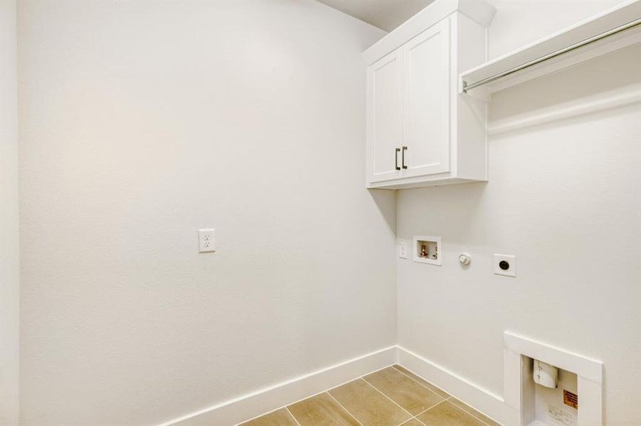 Laundry area featuring neutral-toned tile flooring, crisp white walls, built-in cabinetry with dark hardware, a hanging rod, and utility hookups