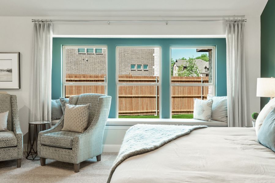 Bedroom with teal accent wall, triple windows, built-in window seat, and accent chairs on carpet