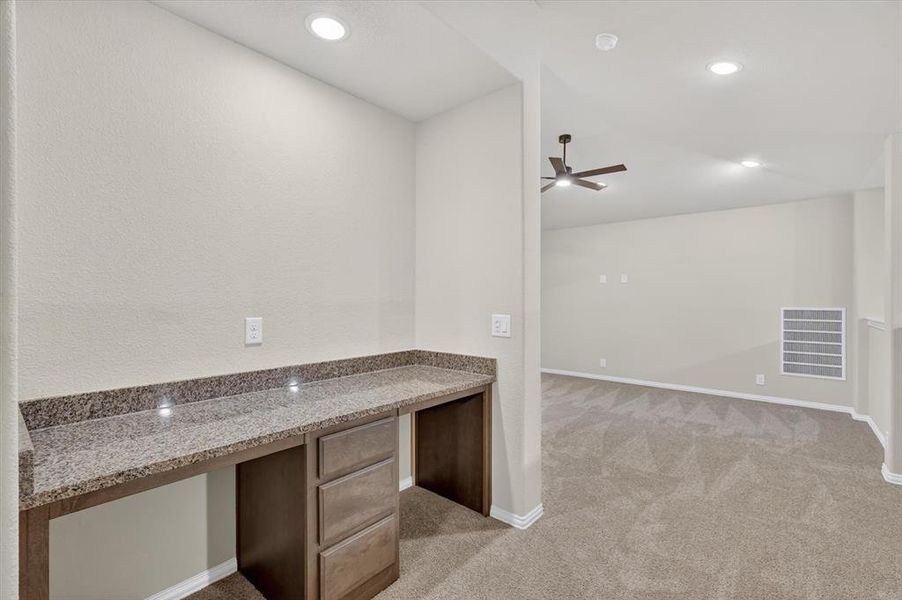 Built-in desk featuring a stone countertop and wood-finish cabinetry, illuminated by recessed lighting Built-in desk featuring a stone countertop and wood-finish cabinetry, illuminated by recessed lighting