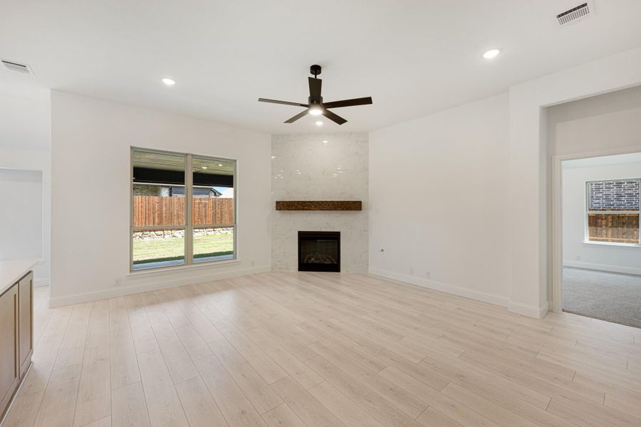 Open living room with light wood floors, tile fireplace, wood mantel, and ceiling fan