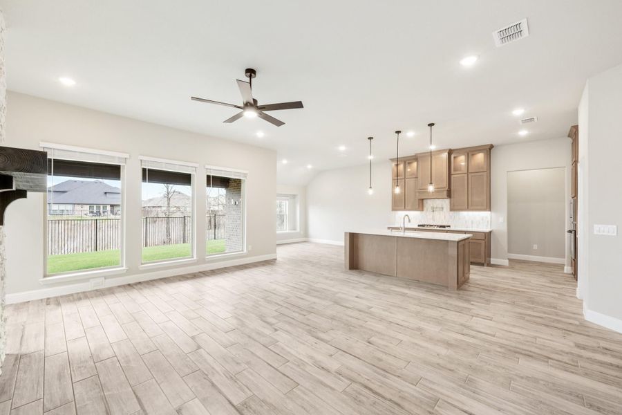 Open-concept living area and kitchen with wood-look tile floors, center island, tan cabinets, and ceiling fan