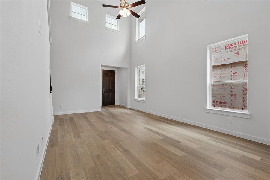 Unfurnished living room with a ceiling fan, light wood-type flooring, baseboards, and a towering ceiling Unfurnished living room with a ceiling fan, light wood-type flooring, baseboards, and a towering ceiling