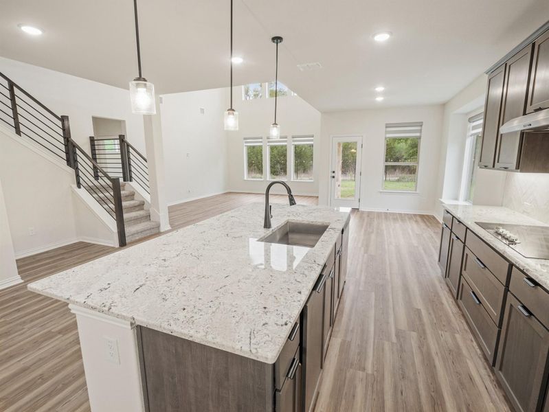 Kitchen featuring light stone countertops, dark wood finish cabinets, and a kitchen island with sink