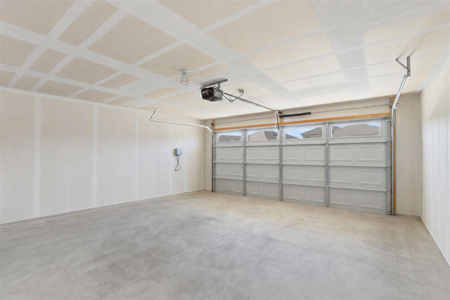 Spacious garage with a sectional overhead door featuring upper window panels, a concrete floor, and an automatic garage door opener