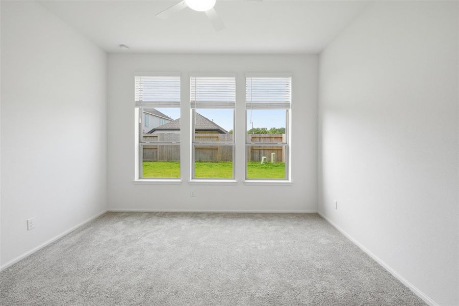 Another bright and spacious room with large windows overlooking a lush backyard, featuring soft carpet and a ceiling fan for comfort.