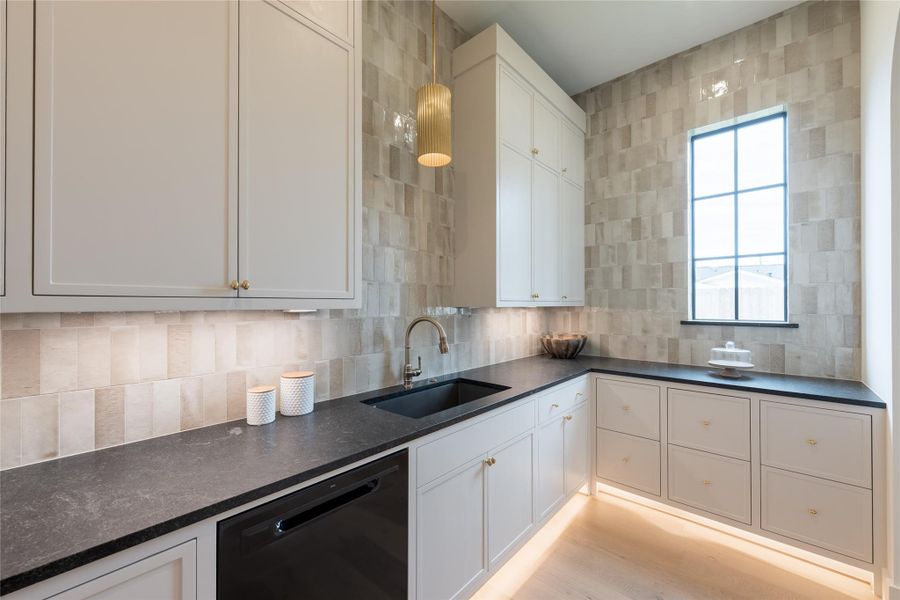 The scullery kitchen is wrapped in softly reflective handmade tile, this prep kitchen blends functionality with high design—complete with black stone countertops, under-cabinet lighting, and custom cabinetry accented by brass hardware. Natural light pours in through a grid-framed window, highlighting the tonal textures and warm ambiance that extend seamlessly from the main kitchen. The scullery kitchen is wrapped in softly reflective handmade tile, this prep kitchen blends functionality with high design—complete with black stone countertops, under-cabinet lighting, and custom cabinetry accented by brass hardware. Natural light pours in through a grid-framed window, highlighting the tonal textures and warm ambiance that extend seamlessly from the main kitchen.