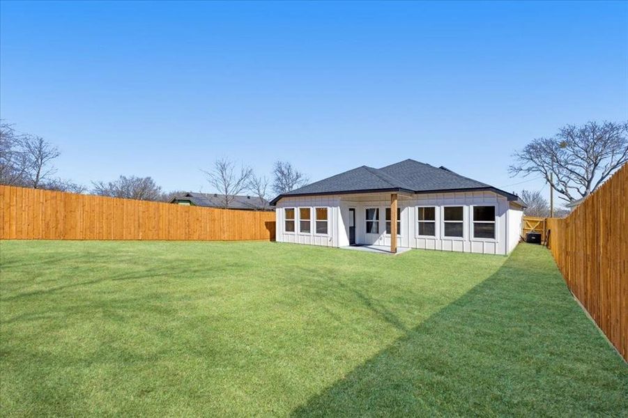 Back of house featuring a yard, a shingled roof, board and batten siding, and a fenced backyard