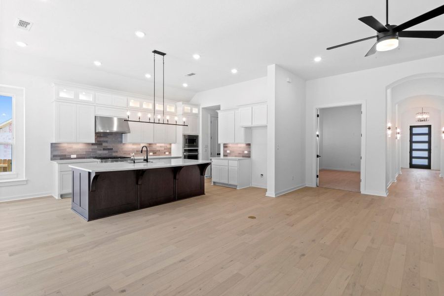 Kitchen with tasteful backsplash, a center island with sink, light wood-style floors, light countertops, and arched walkways