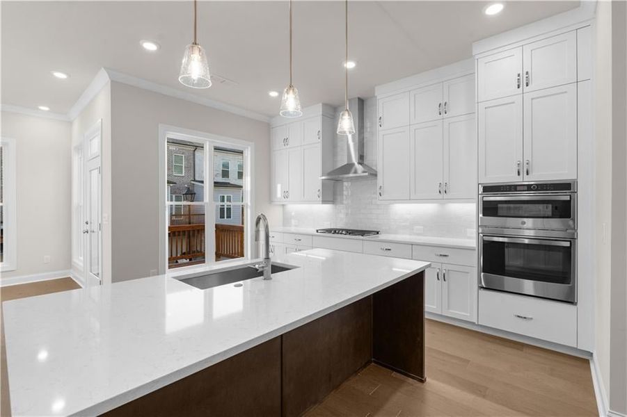 Kitchen featuring light wood-style floors, wall chimney range hood, recessed lighting, dark brown cabinetry, and stainless steel appliances