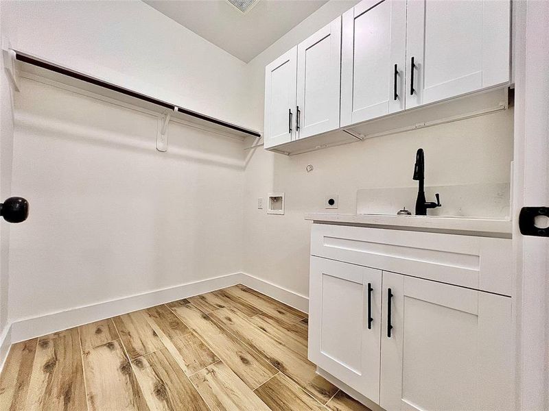 Laundry Room Also has Modern White Shaker Cabinets to Maximize Storage, Black Faucet and Hardware, Hanging Rod And LED Lighting.