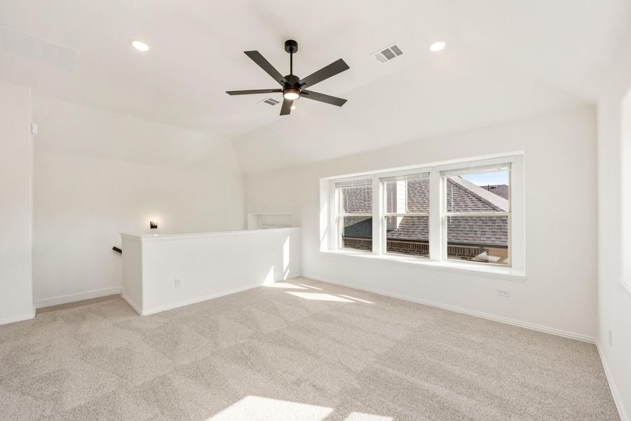 Empty upstairs loft with vaulted ceiling, ceiling fan, carpet flooring, and large window
