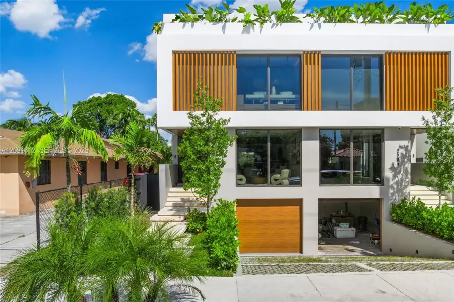 Contemporary two-story exterior featuring a rooftop terrace, wood-slat screening, expansive floor-to-ceiling windows, and a built-in garage with a matching wood-finish door Contemporary two-story exterior featuring a rooftop terrace, wood-slat screening, expansive floor-to-ceiling windows, and a built-in garage with a matching wood-finish door
