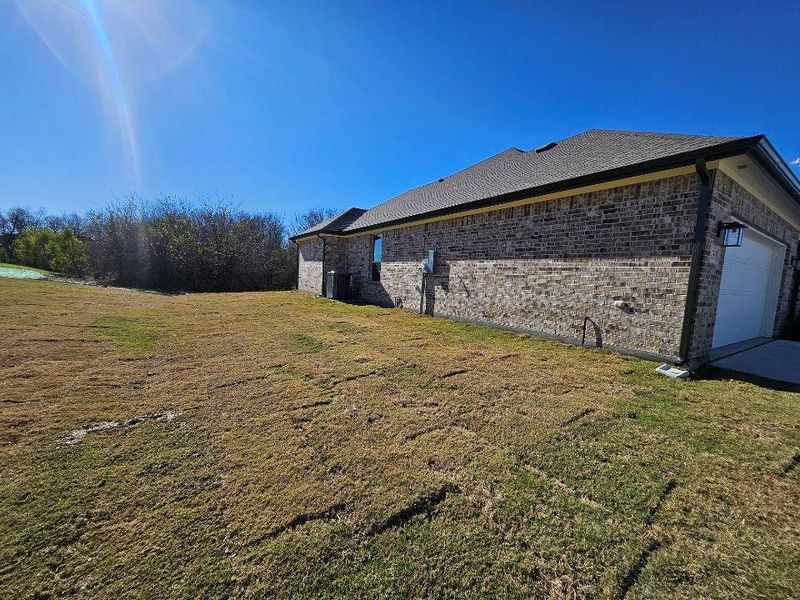 View of home's exterior with brick siding, a lawn, and a garage