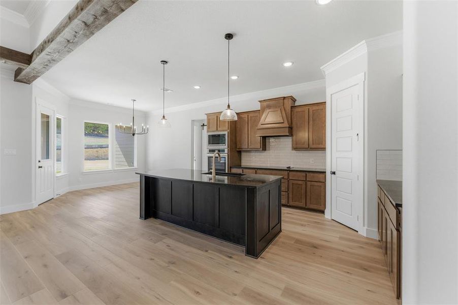 Kitchen with a center island with sink, wood finish cabinets, a chandelier, crown molding, and light wood finished floors