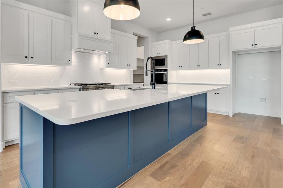 Kitchen with light hardwood / wood-style floors, a kitchen island with sink, and backsplash