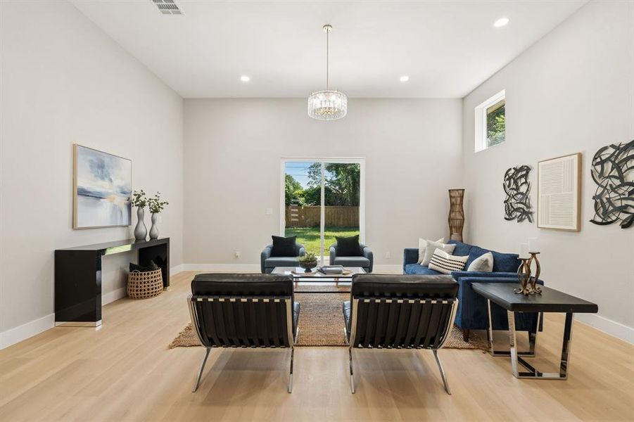 Spacious living area featuring light wood-finish flooring, high ceilings, recessed lighting, and a modern chandelier Spacious living area featuring light wood-finish flooring, high ceilings, recessed lighting, and a modern chandelier