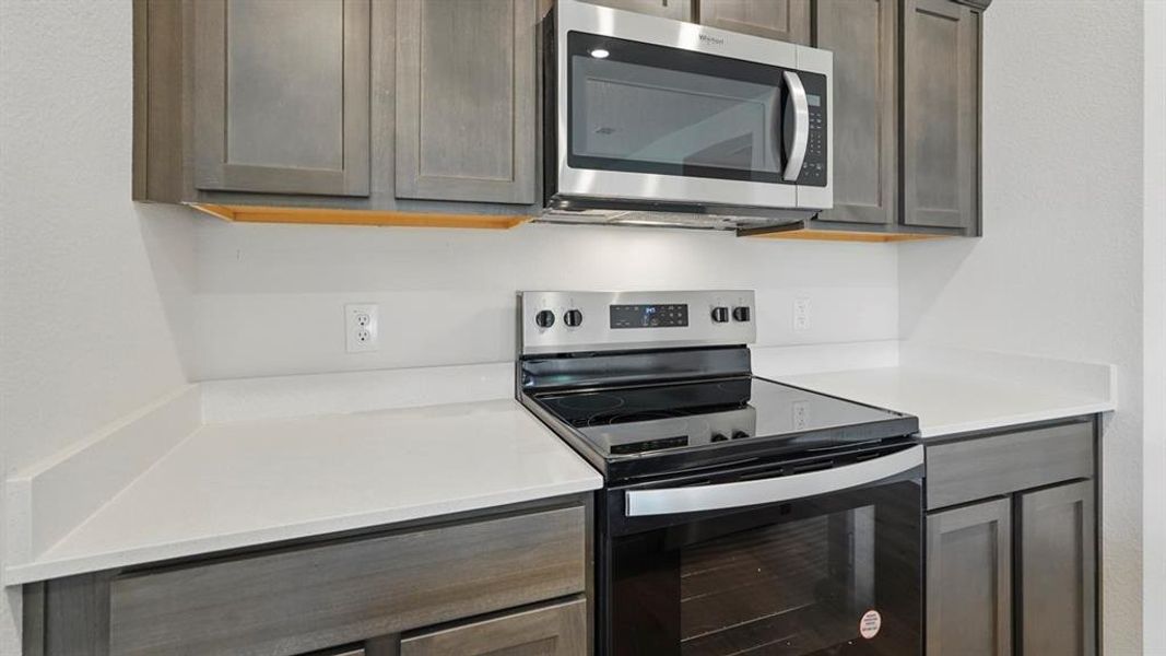Kitchen with appliances with stainless steel finishes, light stone countertops, and dark brown cabinetry