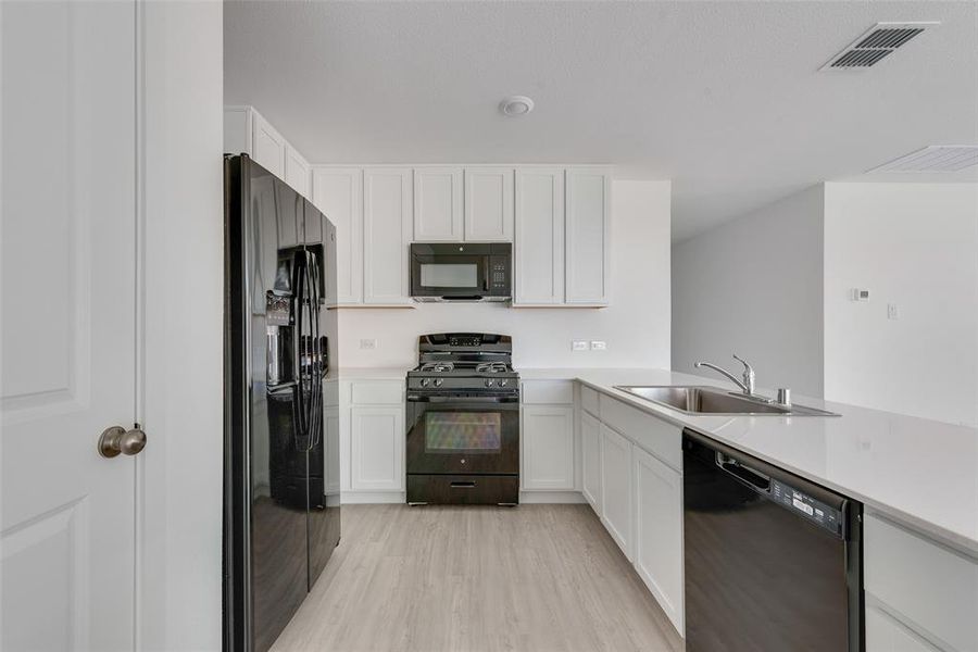 Kitchen with kitchen peninsula, light wood-type flooring, sink, black appliances, and white cabinets