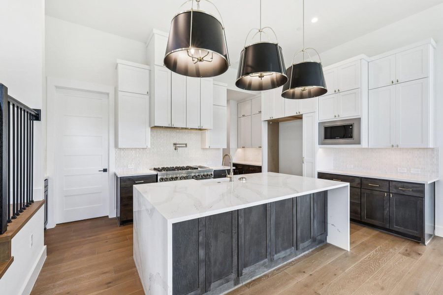 Kitchen featuring white cabinets, light stone counters, decorative backsplash, a center island with sink, and light wood finished floors
